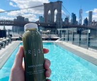 a photo of a bottle of juice in front of the Brooklyn bridge in New York